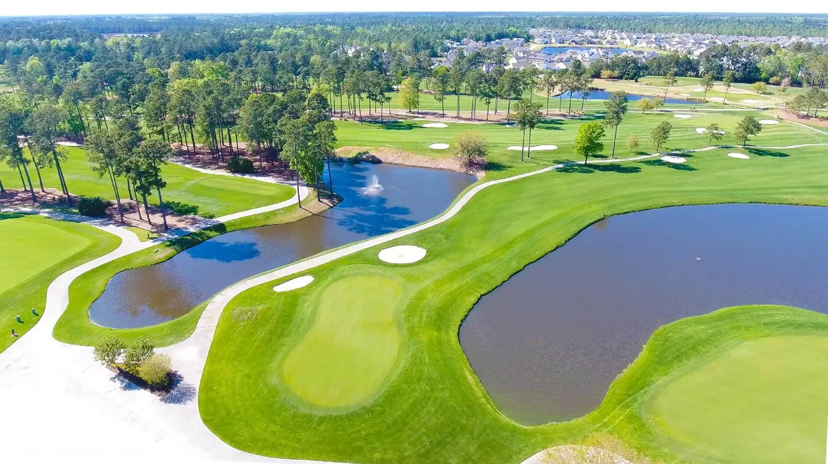 A wide shot of the golf course, with water features and mature trees lining the fairways. The scene conveys the relaxing, open atmosphere and natural beauty that surrounds the course, offering a sense of the outdoor lifestyle available to guests.