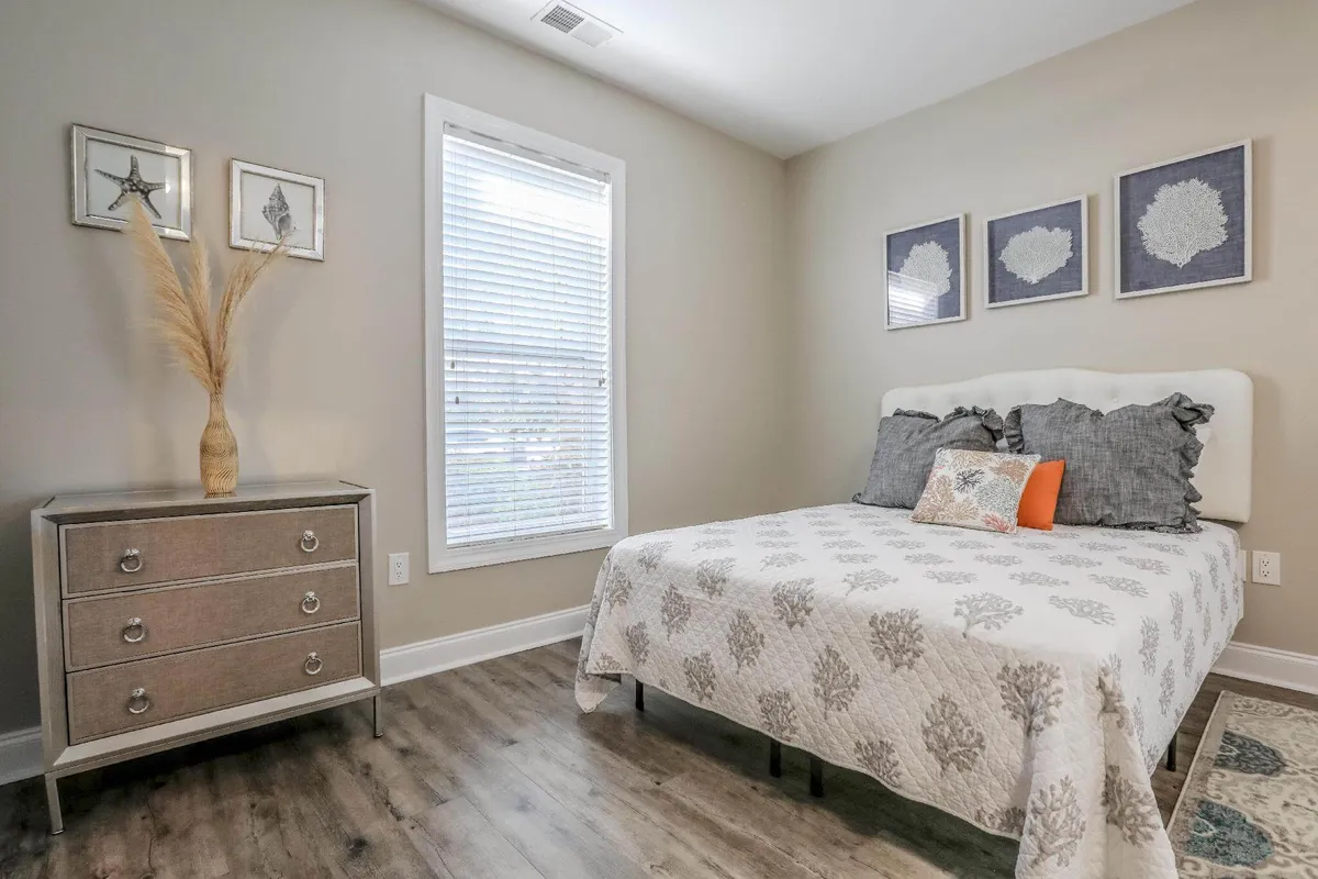 A tranquil bedroom with a cozy bed, nightstand, and soft artwork on the wall. Natural light filters in through a window, creating a calming and restful atmosphere ideal for unwinding after a busy day.