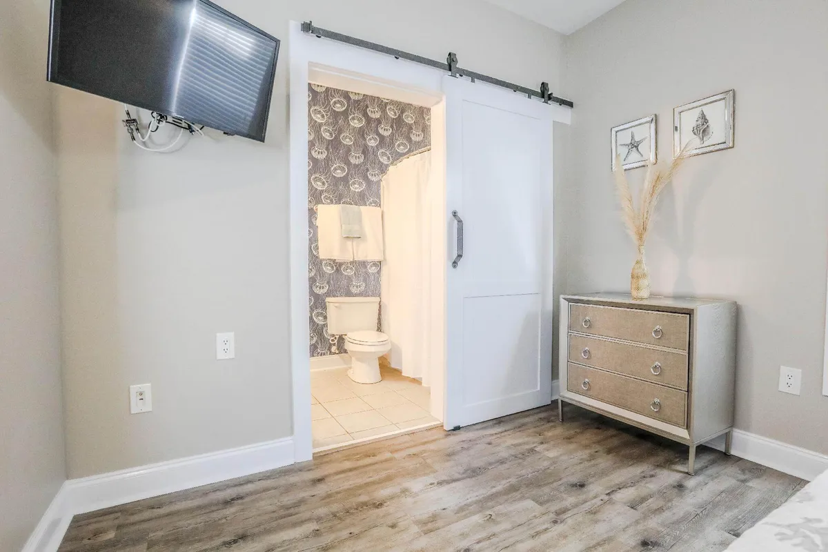 This image shows a cozy interior with the entrance to the bathroom visible from the main living area. The space includes a dresser, television, and soft furnishings, creating a comfortable and inviting environment for getting ready or winding down.