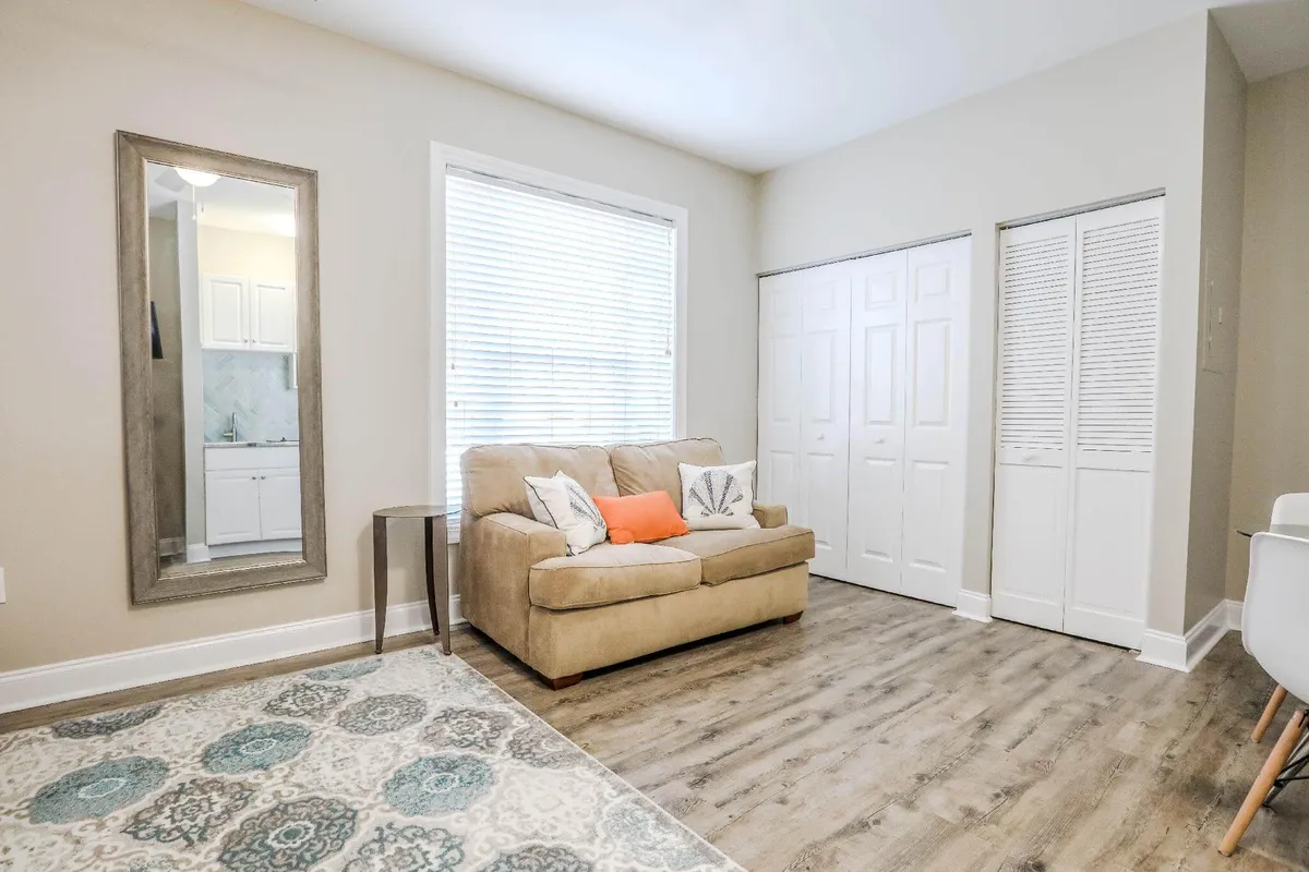 A warm, welcoming living area with a plush sofa, a large mirror reflecting natural light, and a cozy rug. The space is perfect for relaxing together, sharing intimate conversations over coffee, or enjoying a quiet morning start.