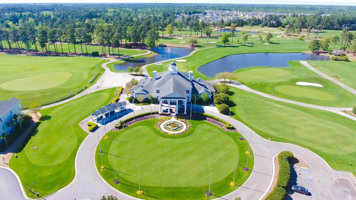 An exterior view of the grand clubhouse set amid manicured lawns, water features, and landscaped gardens, with glimpses of the golf course beyond. The setting exudes luxury, relaxation, and the exclusive social experiences available to residents.