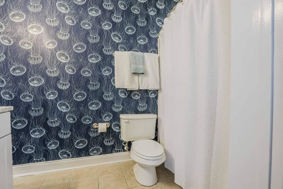 This image features a serene private bath with jellyfish-patterned wallpaper, a white shower curtain, and light-colored tiles. The space is bathed in soft, tranquil lighting that invites relaxation and self-care. The design details evoke a sense of calm and luxury, ideal for a spa-like retreat.